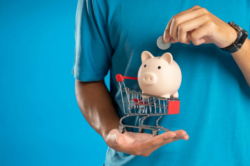Man putting coin in piggy bank in small shopping cart for budget savings