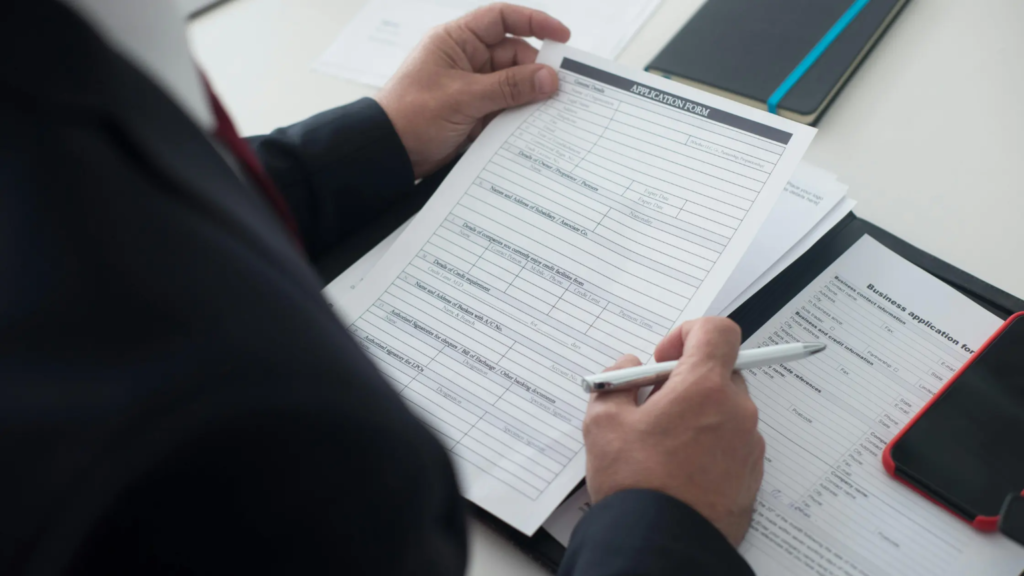 Person completing a phone plan application form with documents and pen